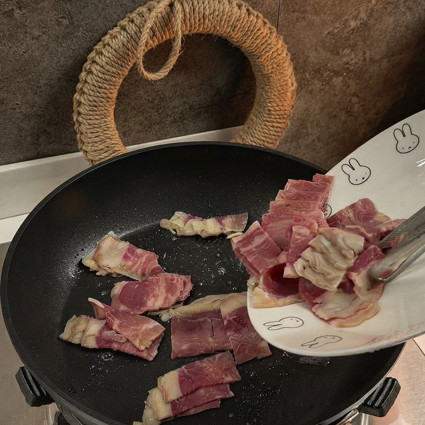Trozos de tocino cortados siendo agregados y salteados en una sartén negra.