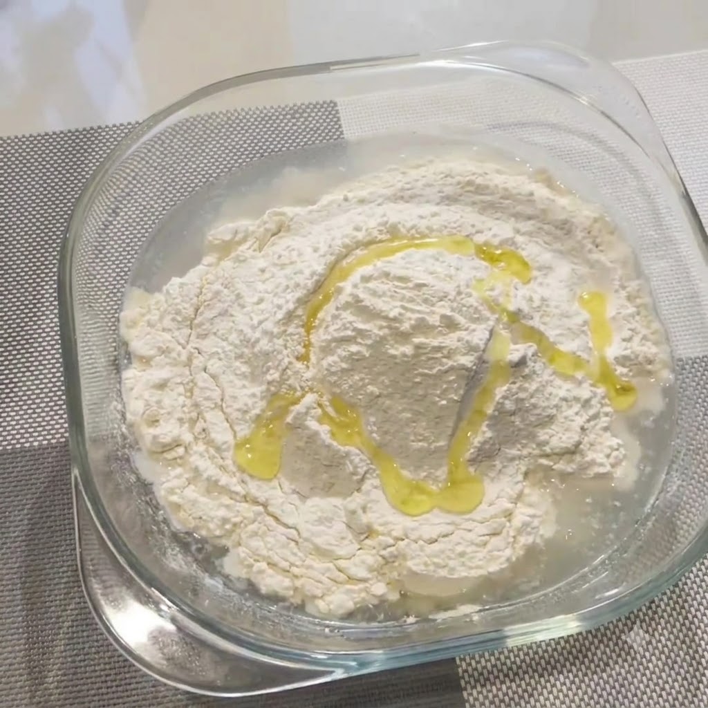 Aceite de oliva rociado sobre harina y agua en un bol de cristal.