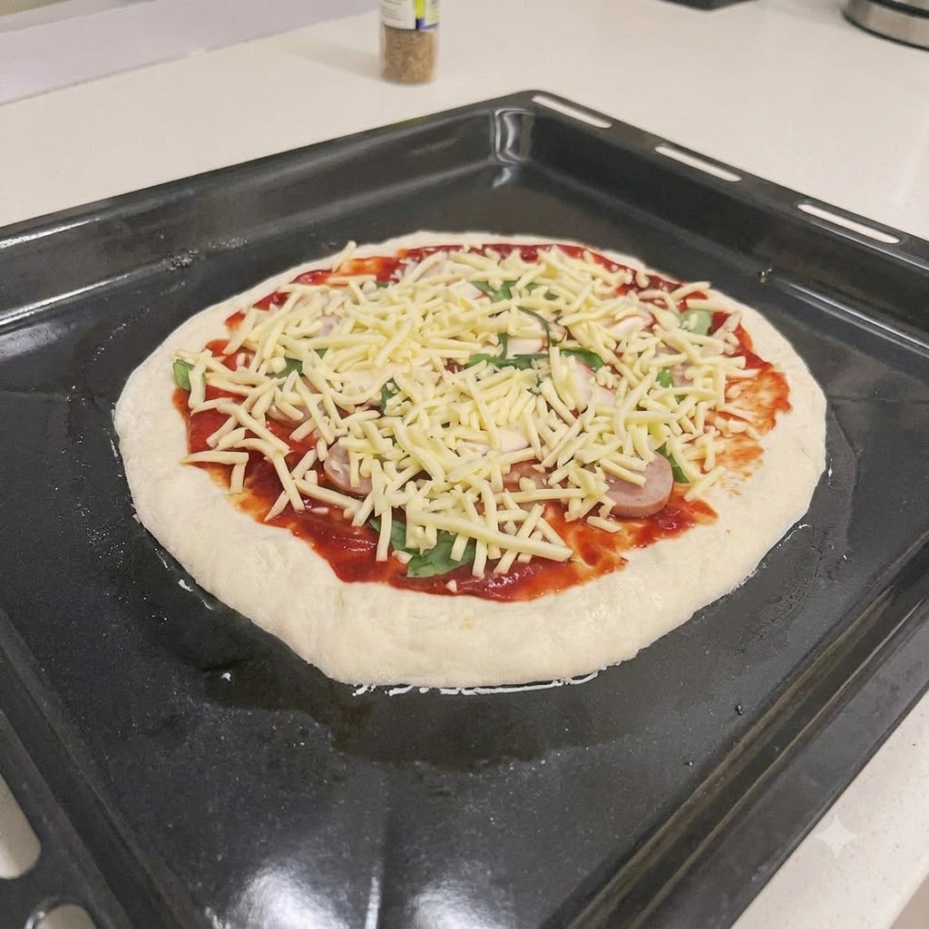 Una pizza sin hornear cubierta con salsa roja, rodajas de salchicha, albahaca fresca y queso rallado en una bandeja de horno negra.