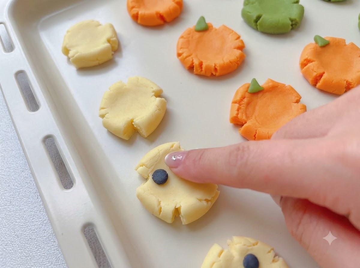 Pequeñas piezas de masa colorida siendo adheridas a bases de galleta aplanadas para formar diseños espeluznantes.