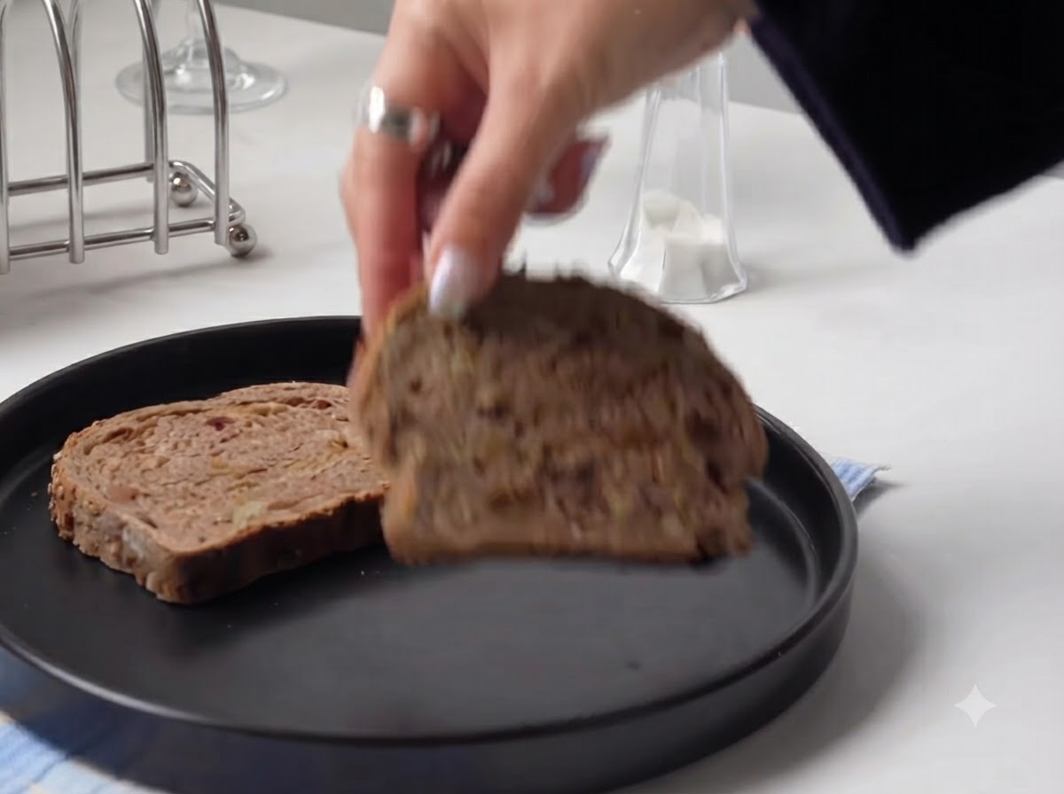 Una mano colocando una rebanada gruesa de pan rústico en un plato negro redondo.
