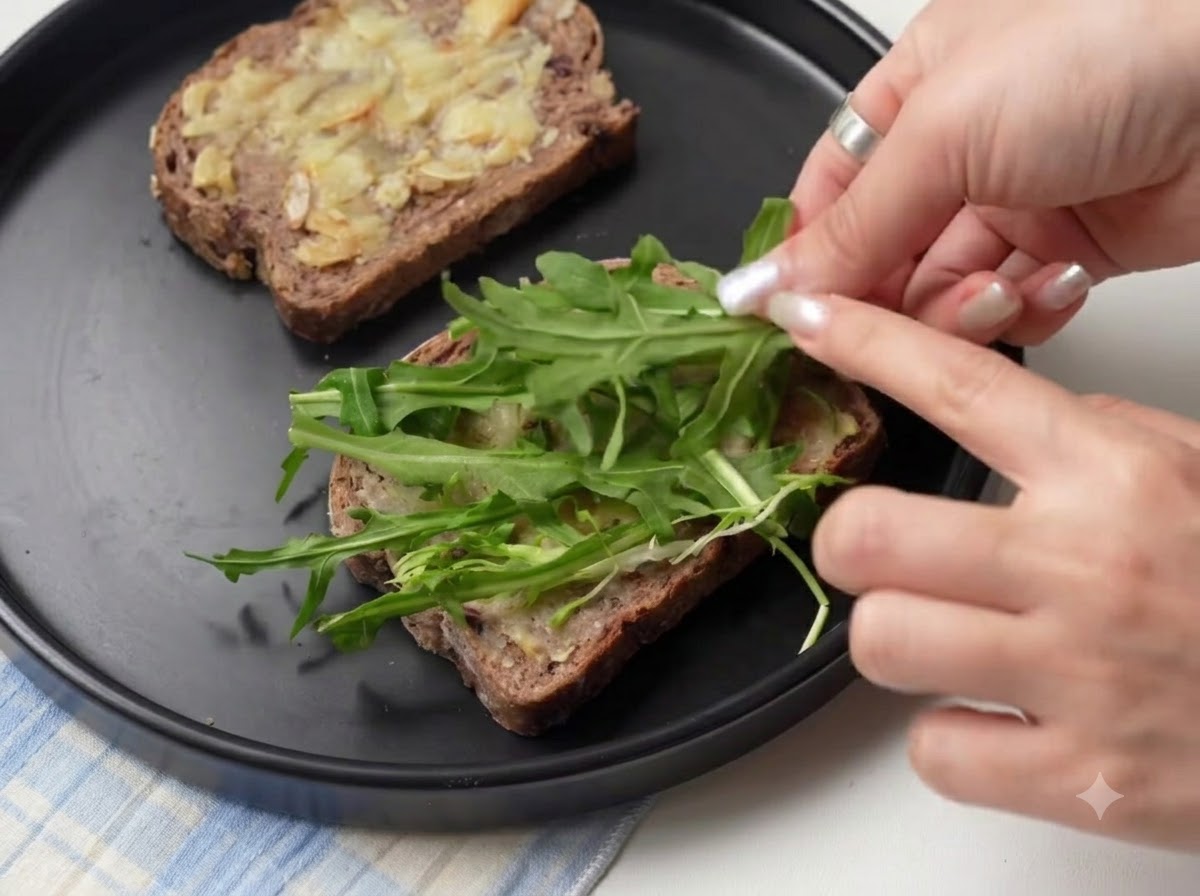 Hojas de rúcula verde fresca colocadas sobre rebanadas de pan untadas con ajo asado.