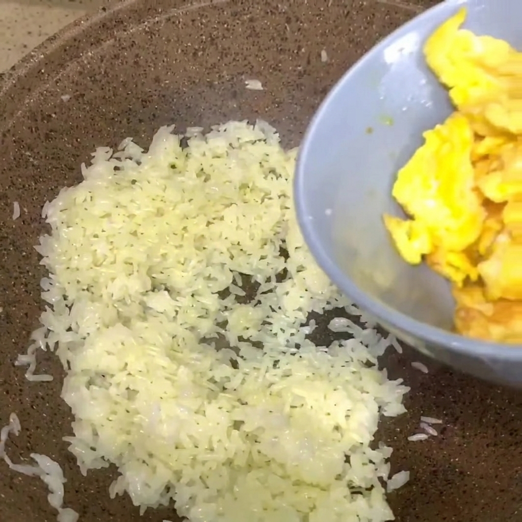 Huevos revueltos vertiéndose en una sartén de arroz blanco cocido.