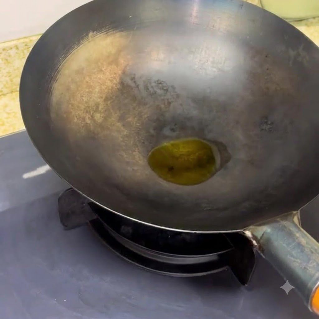 Un wok negro sobre el quemador de una cocina con un poco de aceite calentándose en su interior.