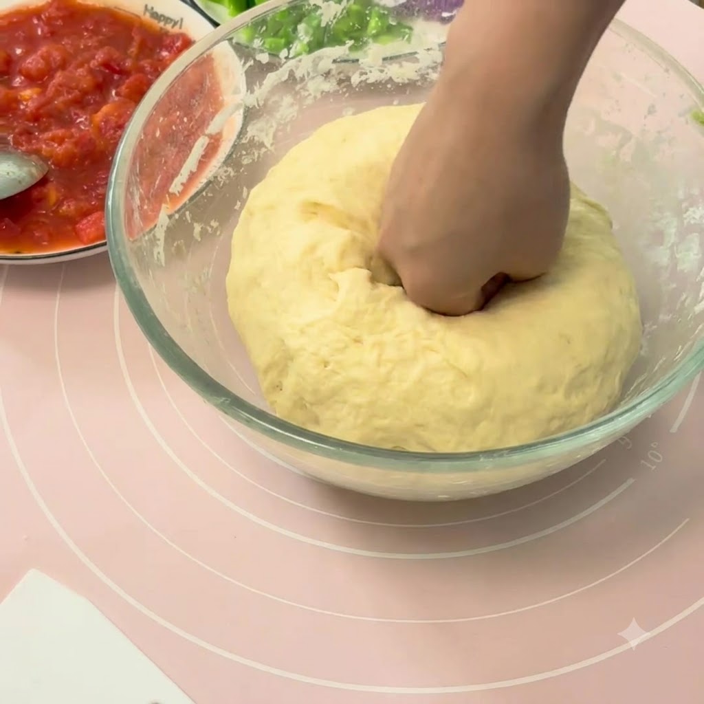 Una mano presionando una gran bola de masa de pizza fermentada dentro de un bol de cristal.