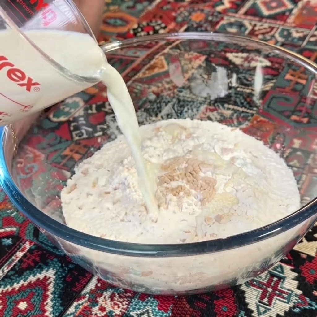 Leche siendo vertida desde una taza medidora de vidrio transparente en un bol con harina y levadura.