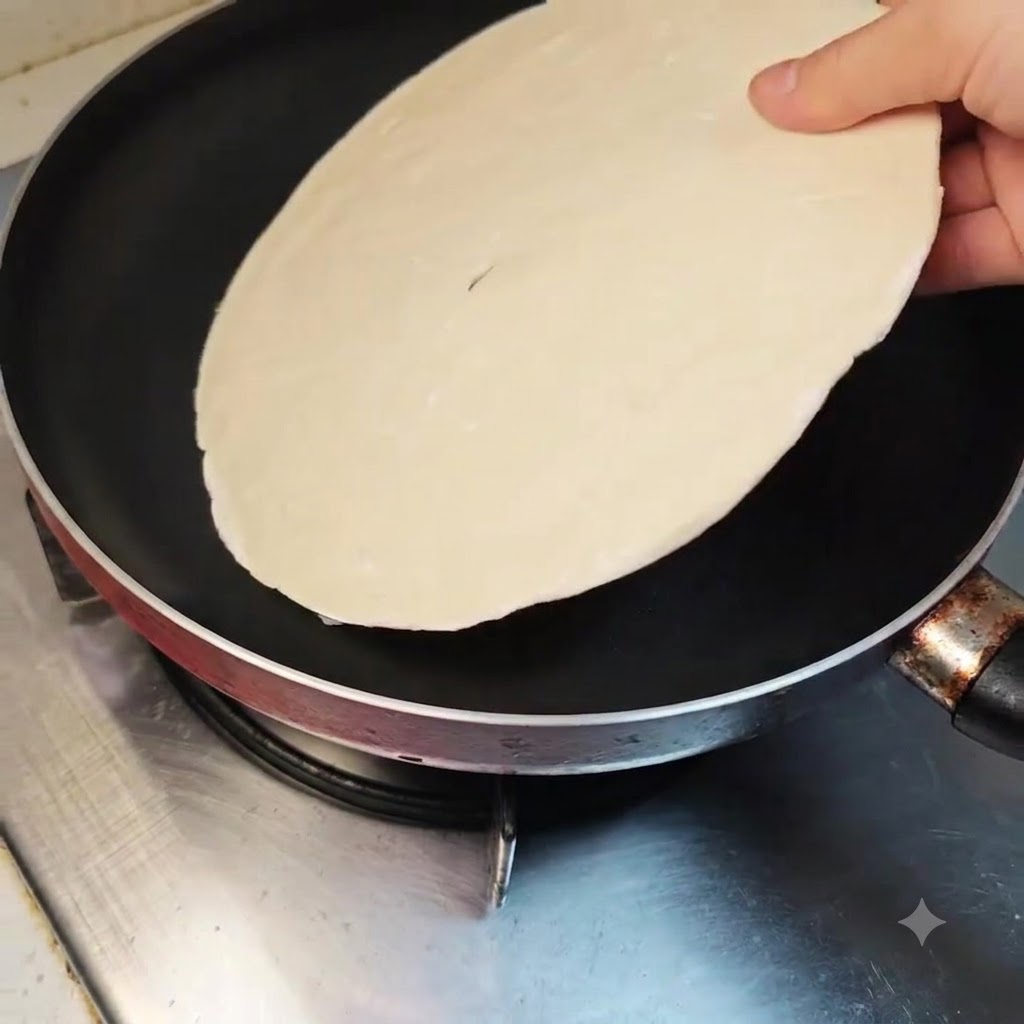 Un panqueque de cebollino colocado plano dentro de una sartén antiadherente limpia en una estufa apagada.