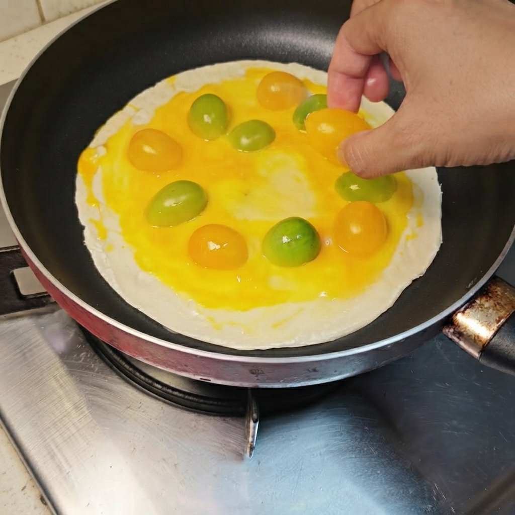 Tomates cherry amarillos y anaranjados siendo organizados en un patrón circular sobre el panqueque cubierto de huevo.