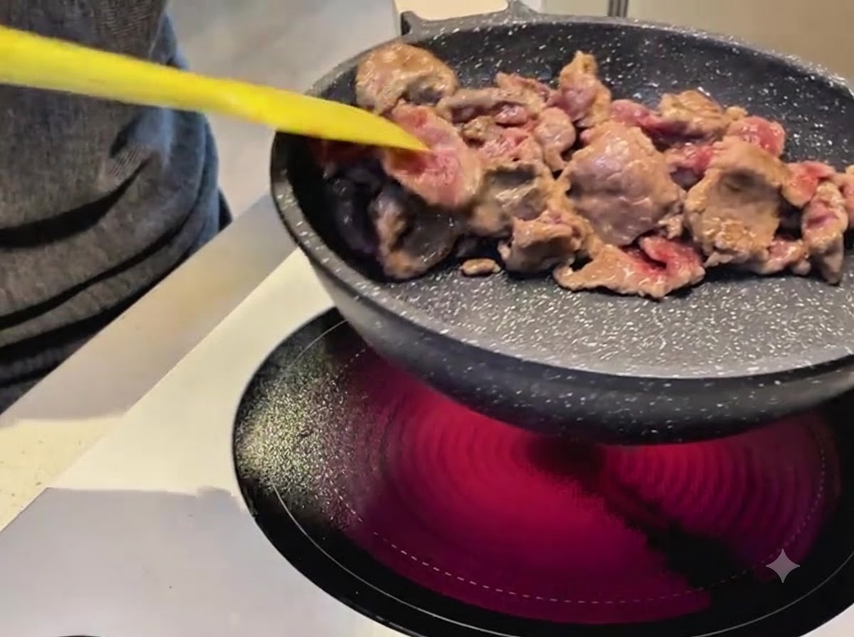 Usando una espátula amarilla para saltear tiras de ternera en una sartén antiadherente sobre una estufa eléctrica.