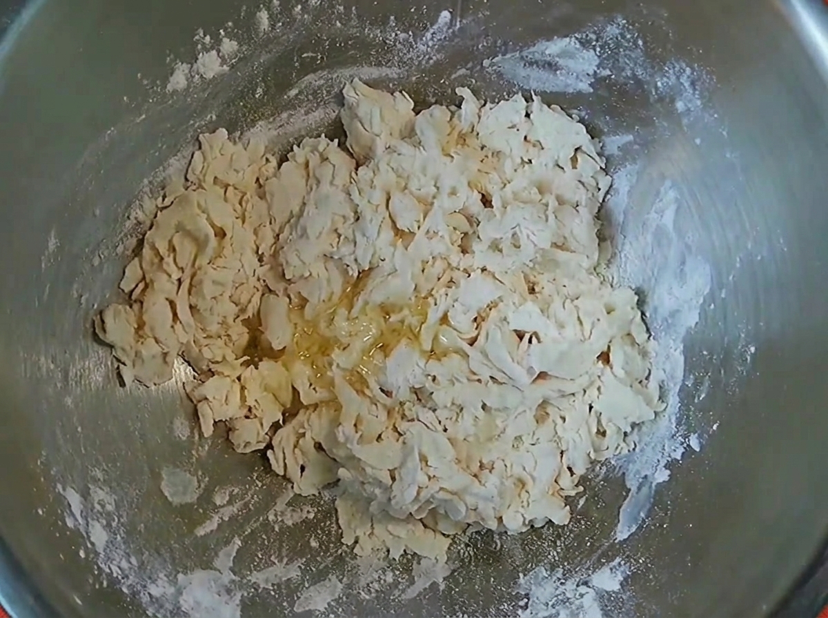 Copos de masa con un chorrito de aceite de cocina dentro de un tazón de mezcla de metal.