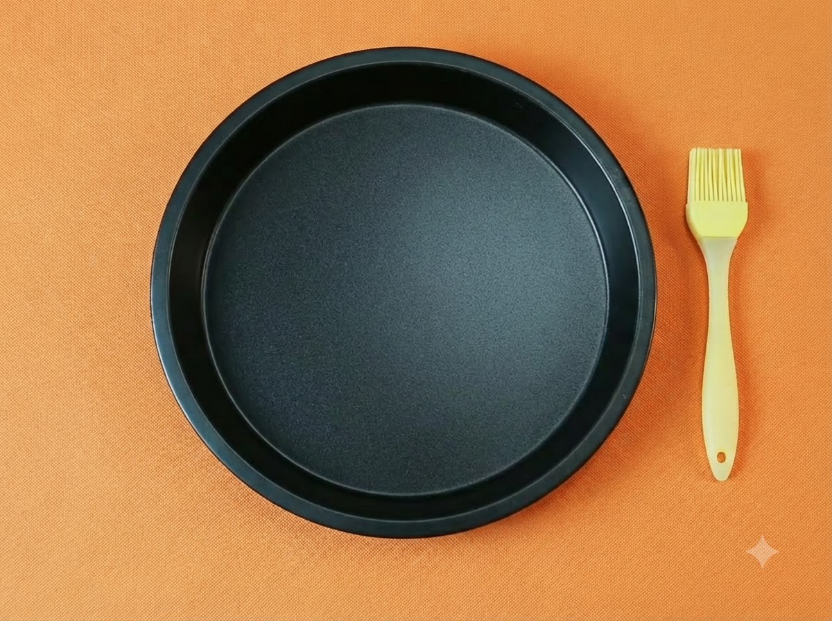 Una sartén para pizza redonda y negra vacía junto con una brocha de silicona amarilla para aceite sobre un fondo naranja.