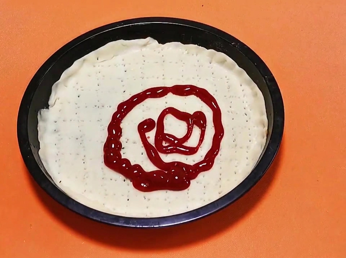 Un patrón en espiral de salsa de tomate de color rojo brillante siendo exprimida en el centro de una base de masa de pizza cruda.