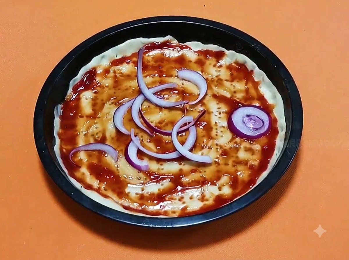 Aros de cebolla roja en rodajas dispuestos sobre una base de masa de pizza con salsa de tomate dentro de un molde para hornear redondo y negro.