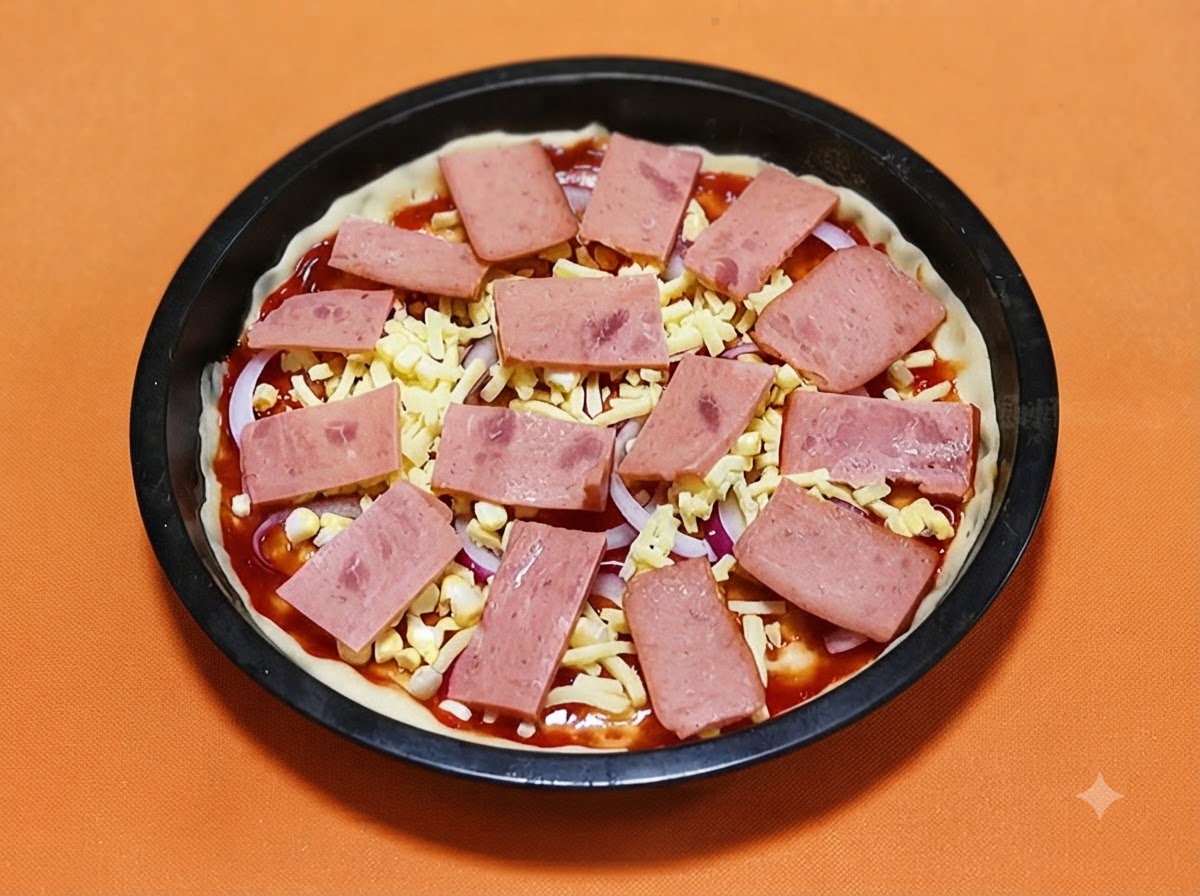 Rodajas rectangulares de jamón rosado dispuestas sistemáticamente sobre una base de pizza cubierta con queso y cebollas.