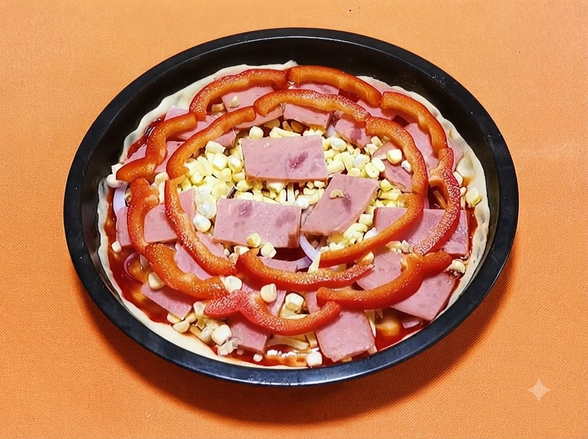 Masa de pizza en una sartén negra cubierta con salsa, jamón, granos de maíz amarillo y rodajas de pimiento rojo.