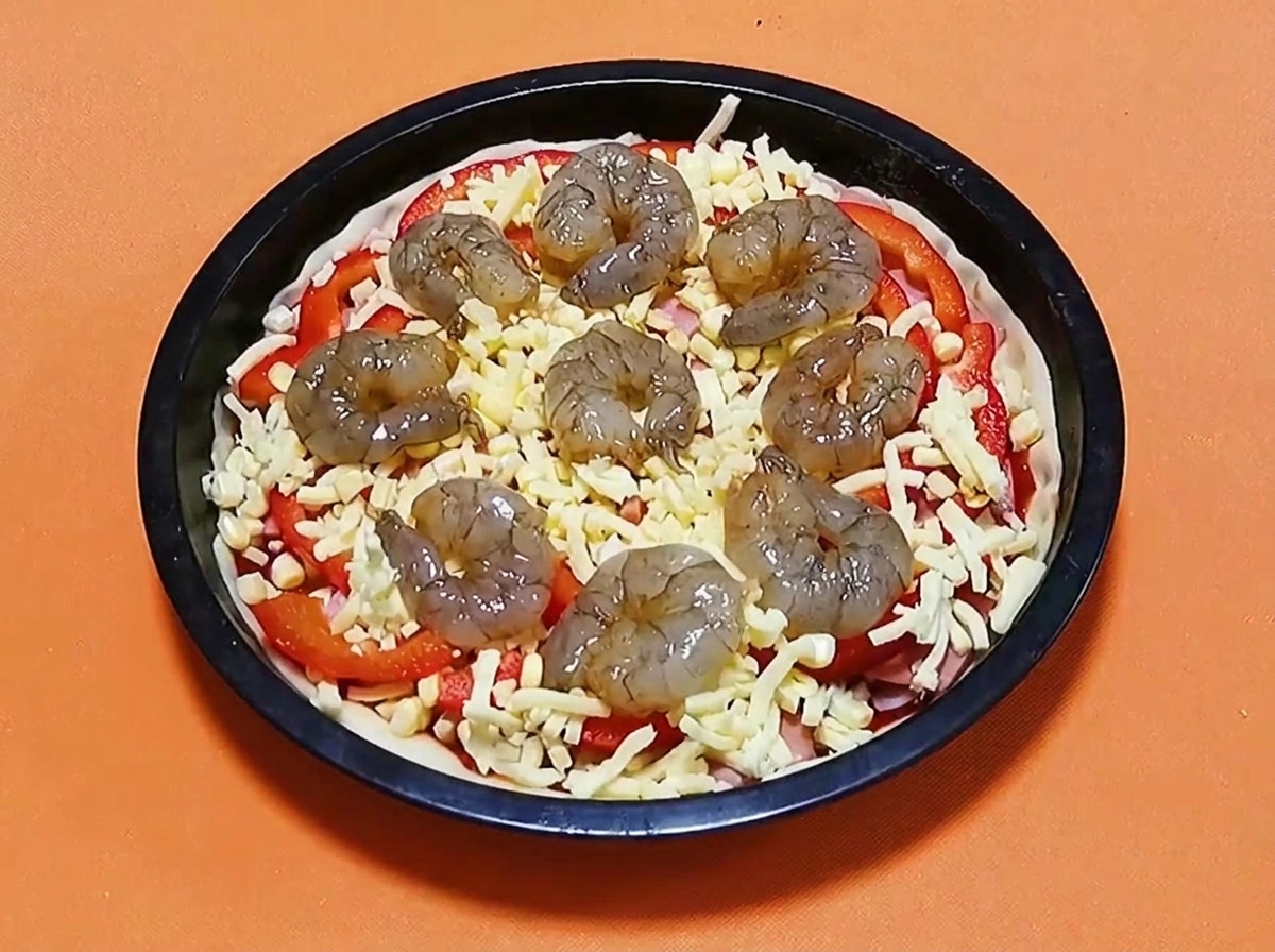 Camarones crudos marinados dispuestos en círculo encima de una pizza con queso, pimientos y jamón.