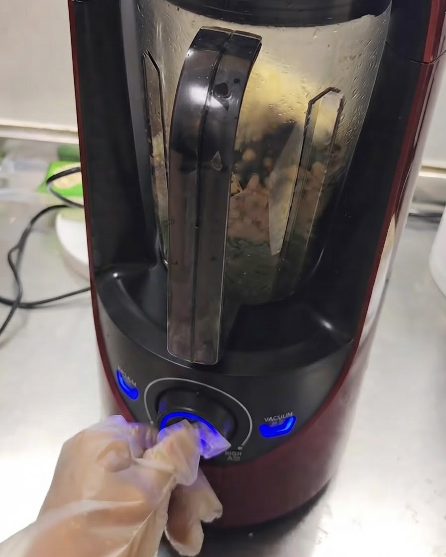 Una licuadora funcionando con ingredientes mezclándose en su interior mientras una mano gira el dial.