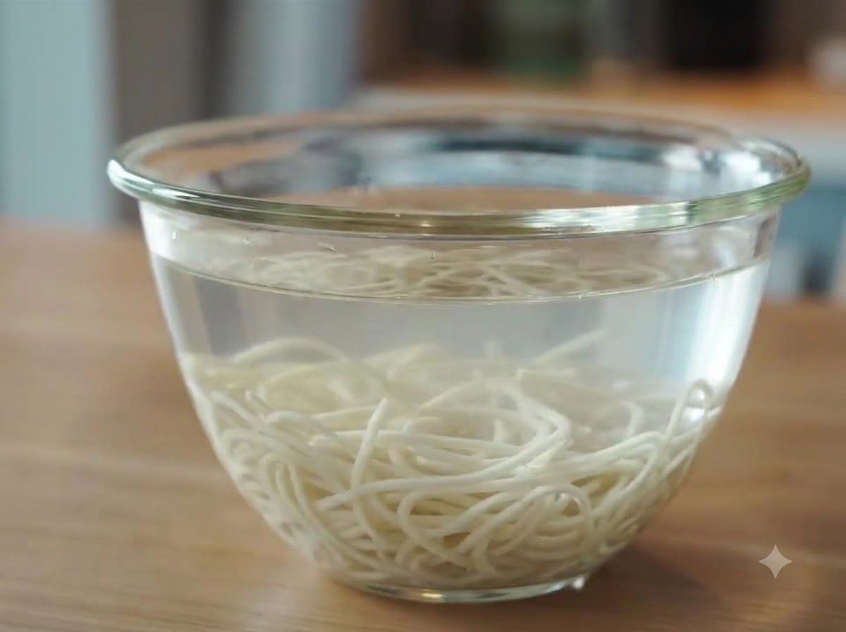 Fideos de ramen recién cocidos sumergidos y enfriándose en un tazón de vidrio lleno de agua fría después de enjuagarse.