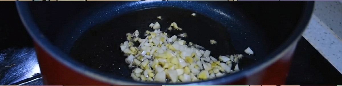 Jengibre y ajo picados friéndose en una olla oscura con aceite de sésamo caliente.