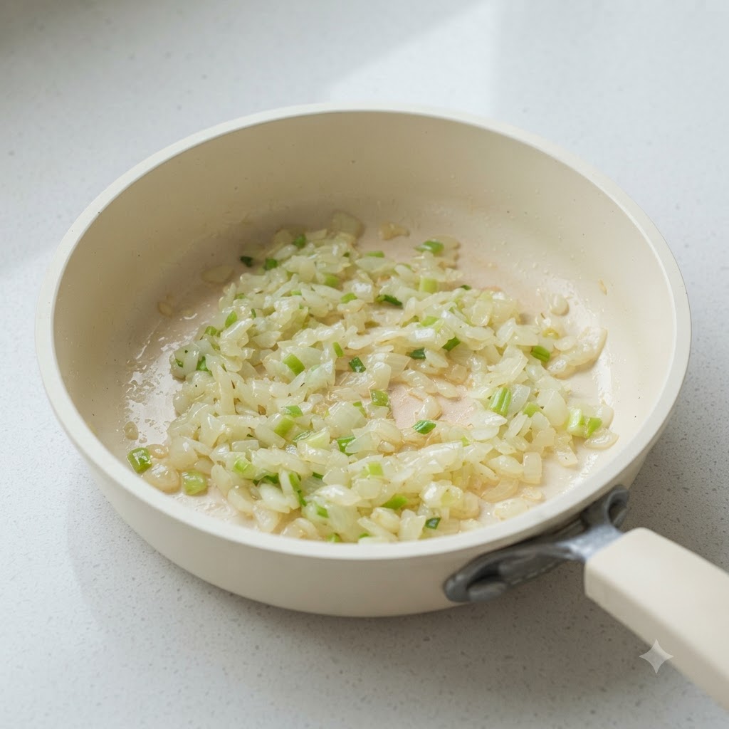 Cebolla picada y partes blancas de cebolleta sofriéndose en una sartén blanca.