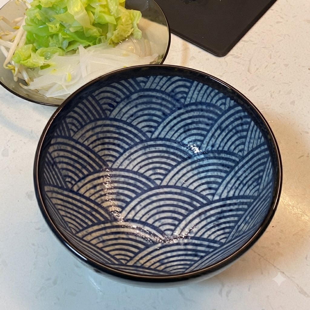 Un tazón de servir con motivos azules colocado junto a un plato de verduras dispuestas.