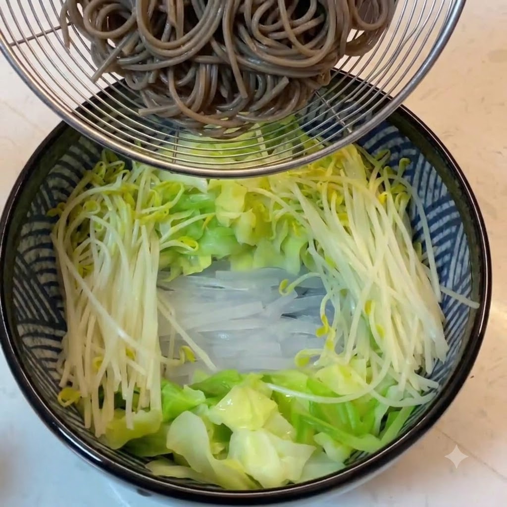 Fideos de trigo sarraceno cocidos sostenidos en un colador de alambre sobre el tazón lleno de verduras.