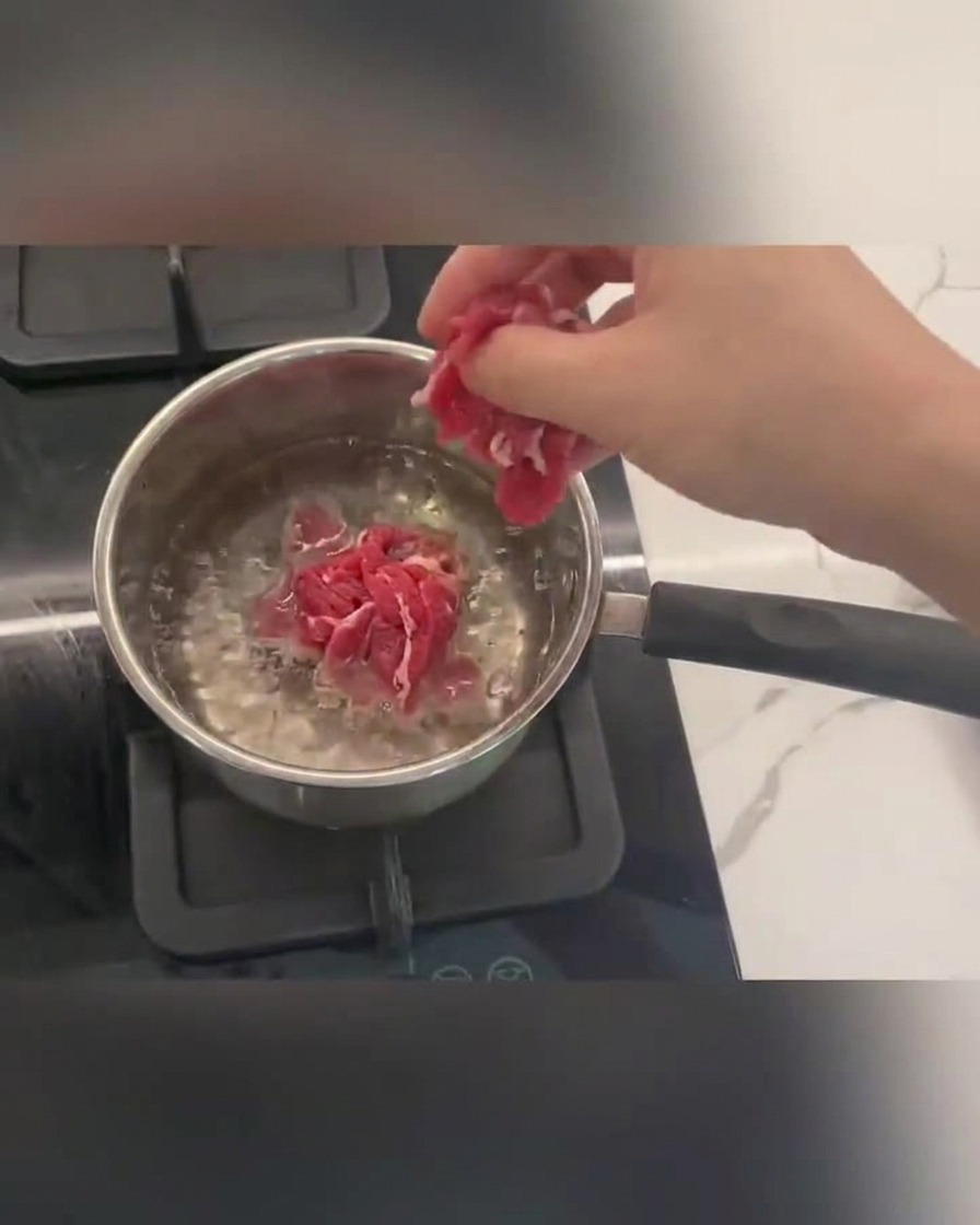 Tiras de ternera cociéndose en agua hirviendo con espuma en la superficie.