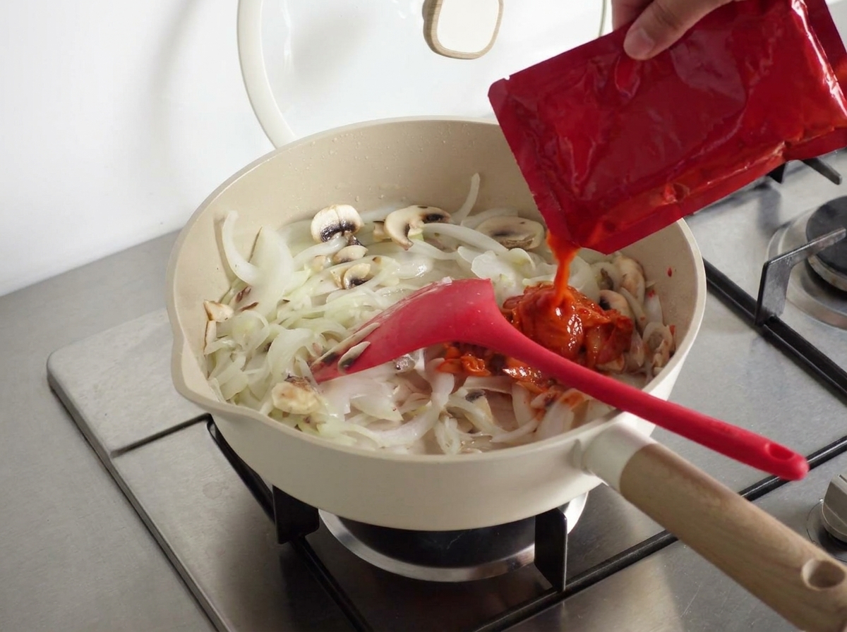 Una cucharada de pasta picante coreana agregándose a la mezcla en la sartén.