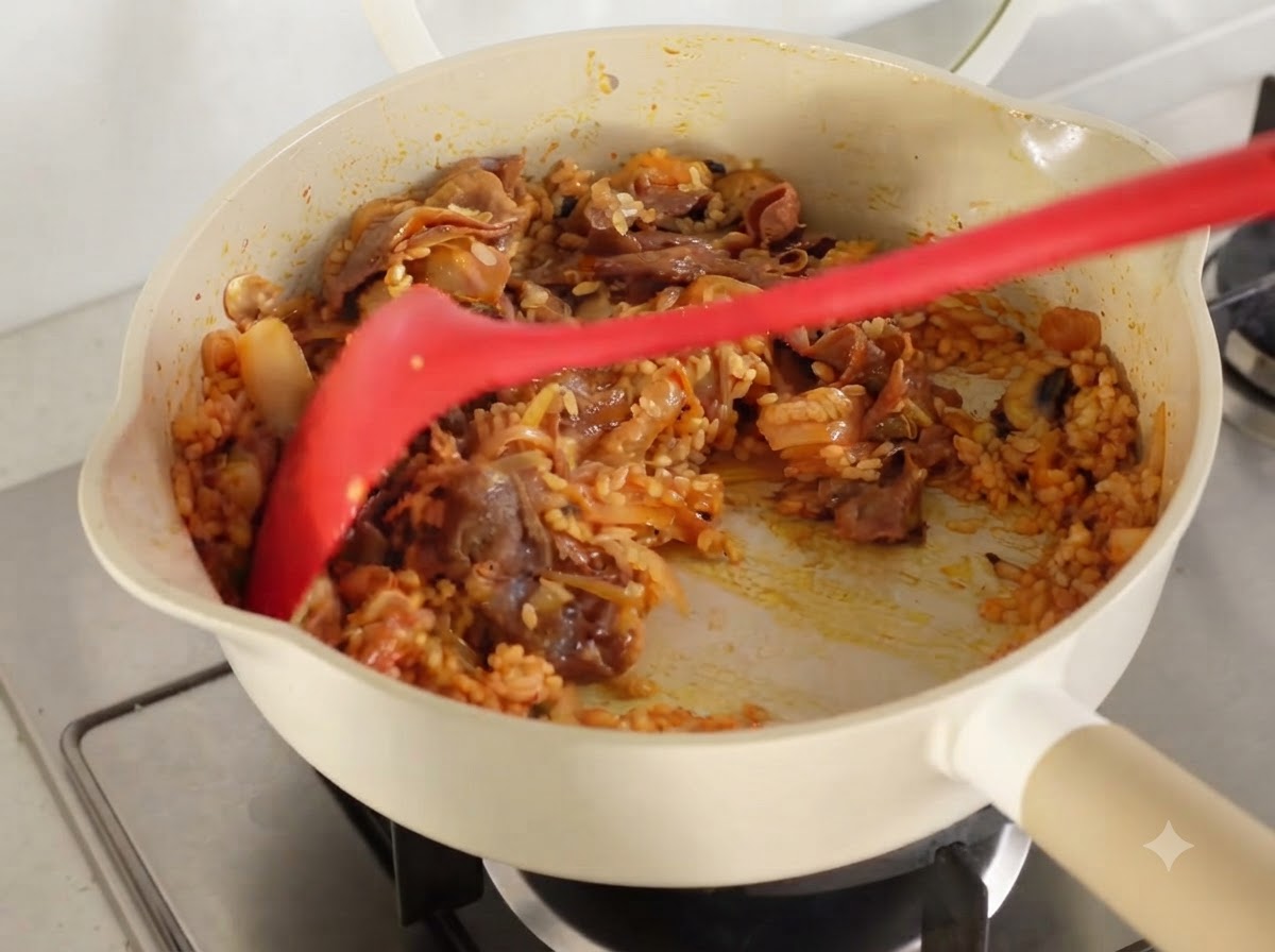 Todos los ingredientes y el arroz salteándose juntos hasta quedar cubiertos con el jugo de kimchi en una sartén.