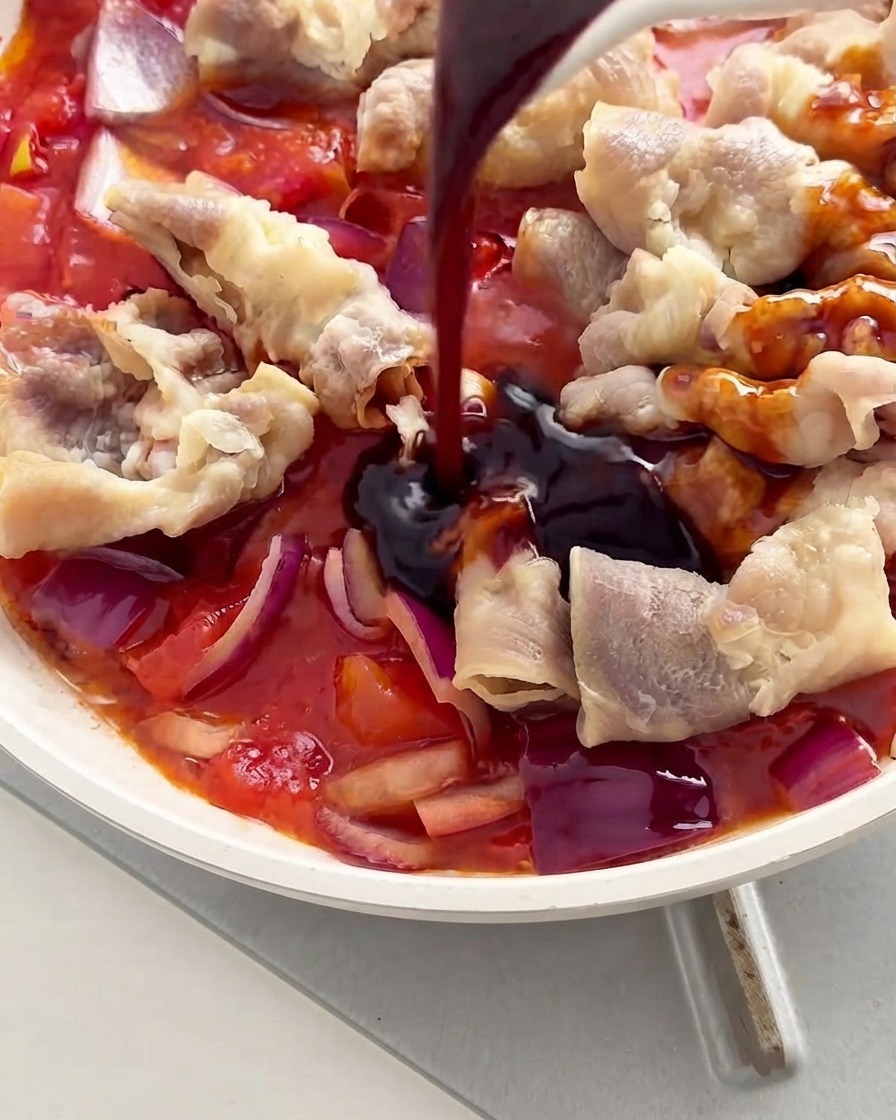 Salsa oscura siendo vertida con una cuchara sobre la carne y los tomates dentro de una sartén blanca.