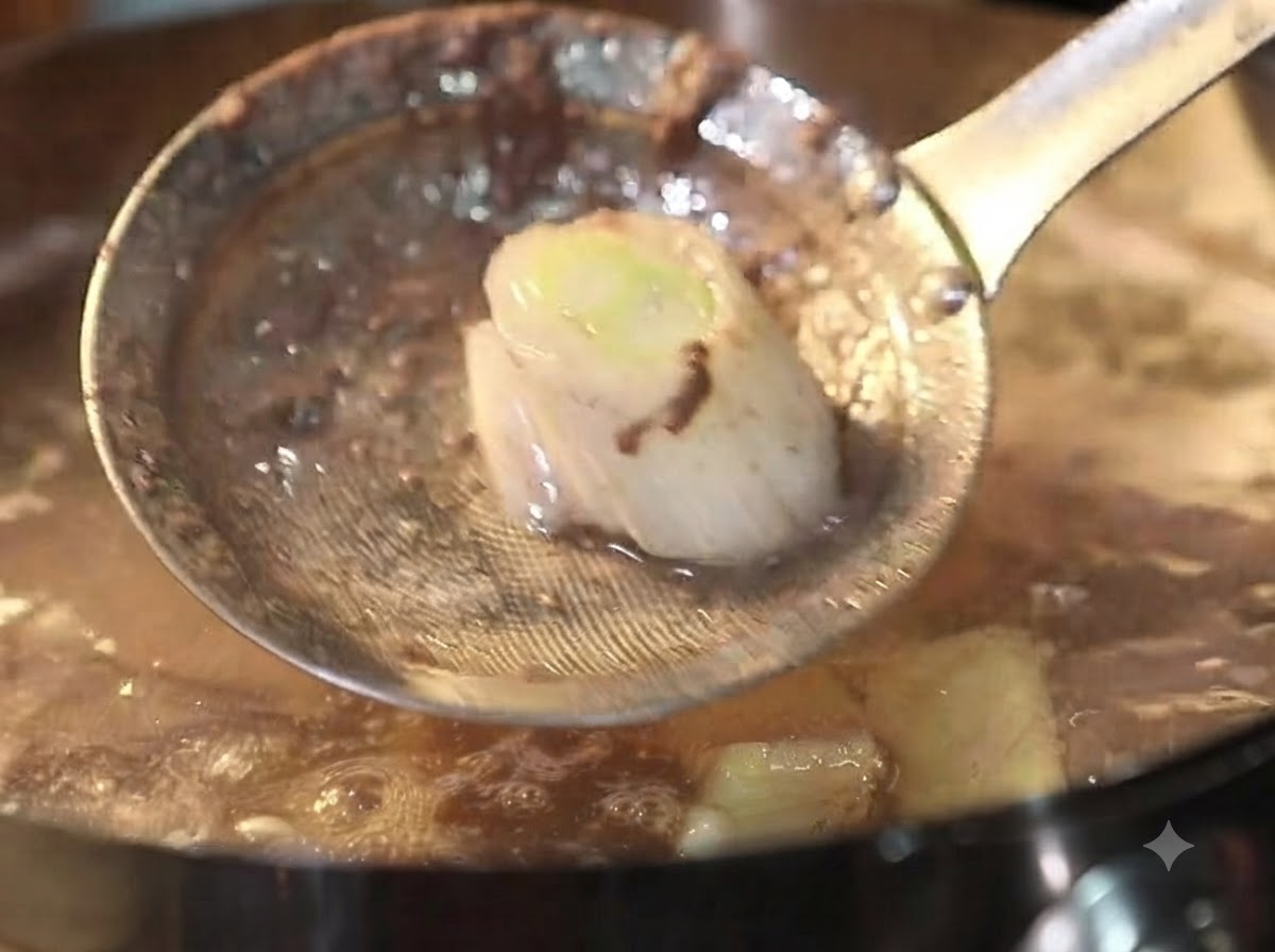 Un colador de metal retirando espuma y residuos de una olla burbujeante con caldo de ternera.