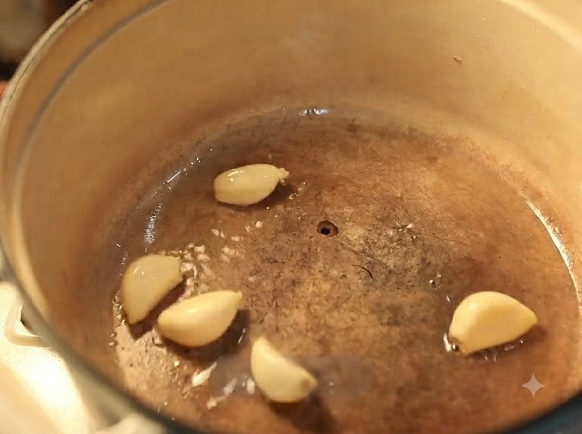 Dientes de ajo friéndose en aceite caliente dentro de una olla de hierro fundido esmaltado.