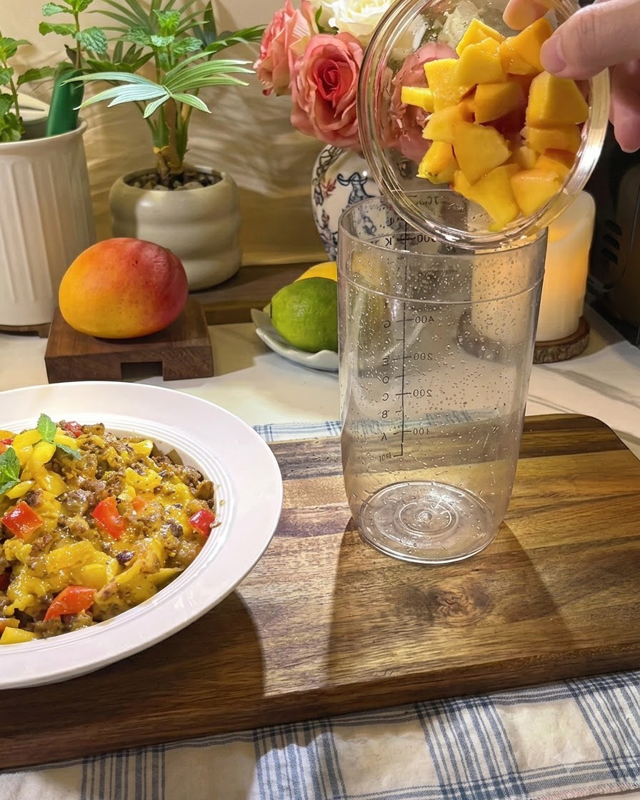 Trozos de durazno fresco, miel y rodajas de limón siendo vertidos en un vaso mezclador alto y transparente.