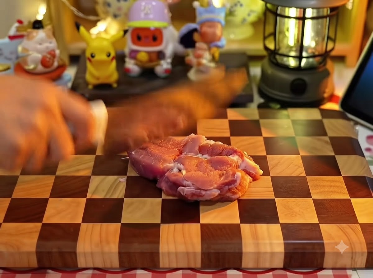 Una mano usando un cuchillo de cocina para hacer cortes en una pieza de carne de cerdo cruda sobre una tabla de picar de madera a cuadros.
