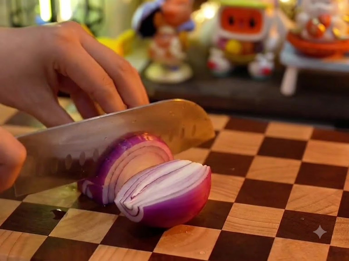 Un cuchillo de cocina cortando una cebolla morada en una tabla de picar de madera a cuadros.