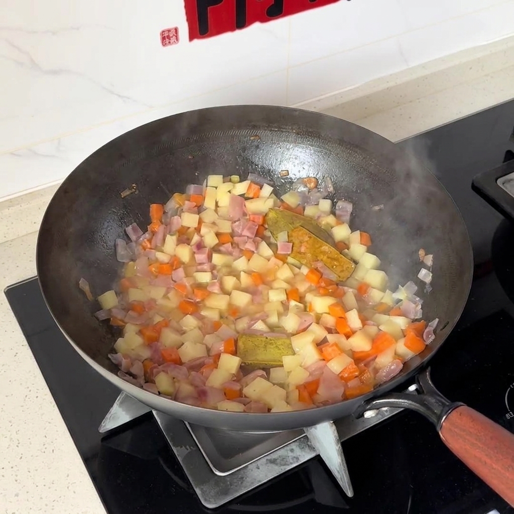 Patatas y zanahorias en dados siendo mezcladas con cebollas dentro de un wok.