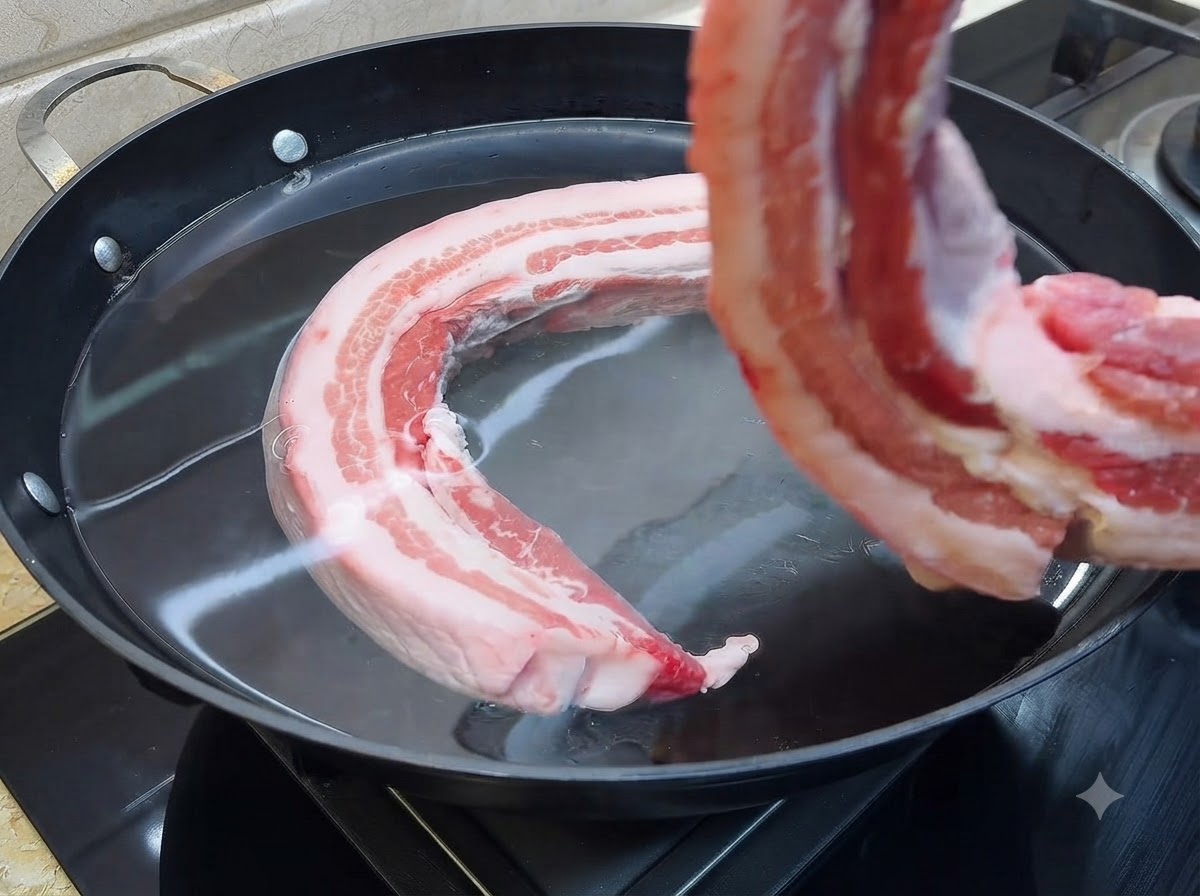 Un trozo de panceta cruda sumergiéndose en una olla grande con agua fría.
