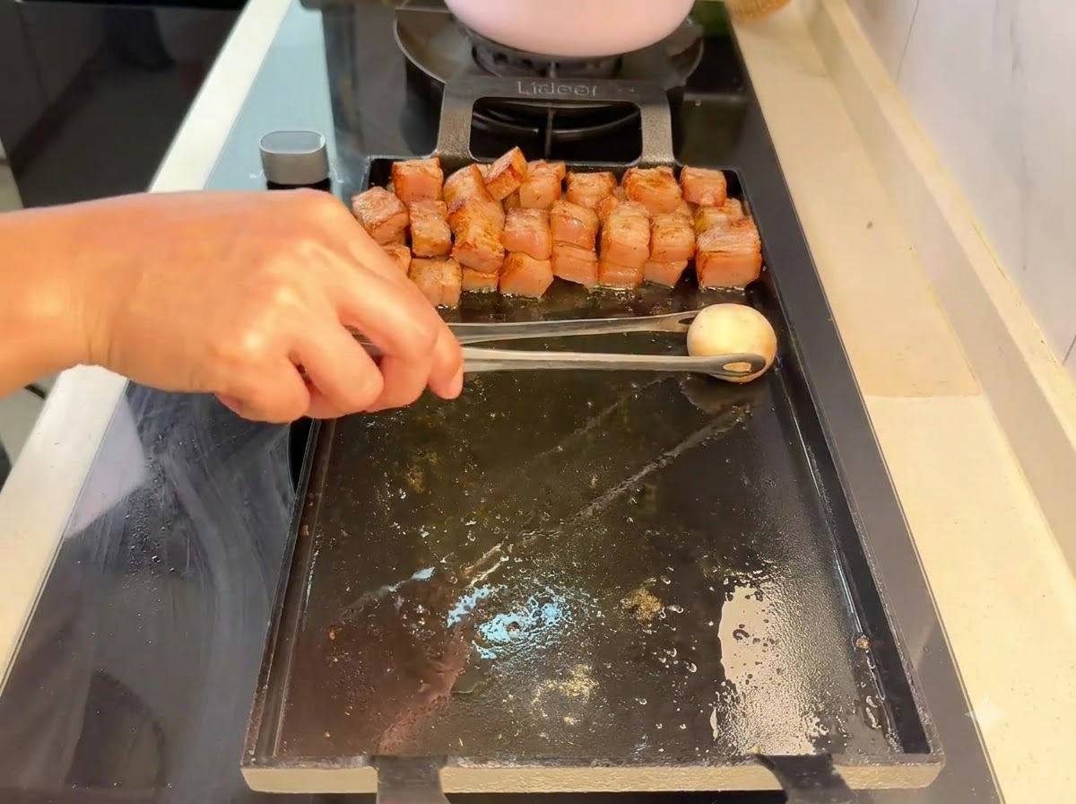 Un champiñón colocándose con pinzas en la parrilla junto a los trozos de cerdo.