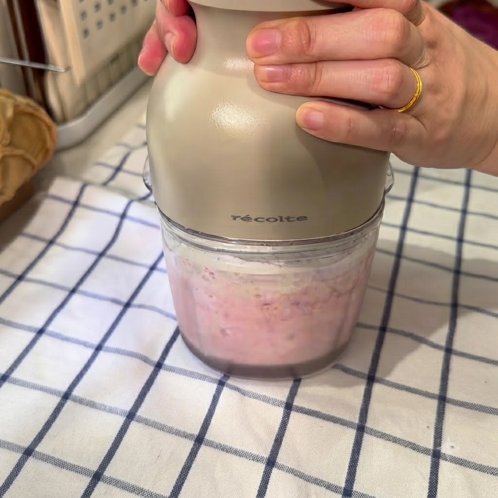 Un procesador de alimentos batiendo una mezcla rosa de sandía congelada, agua con hielo y leche condensada.