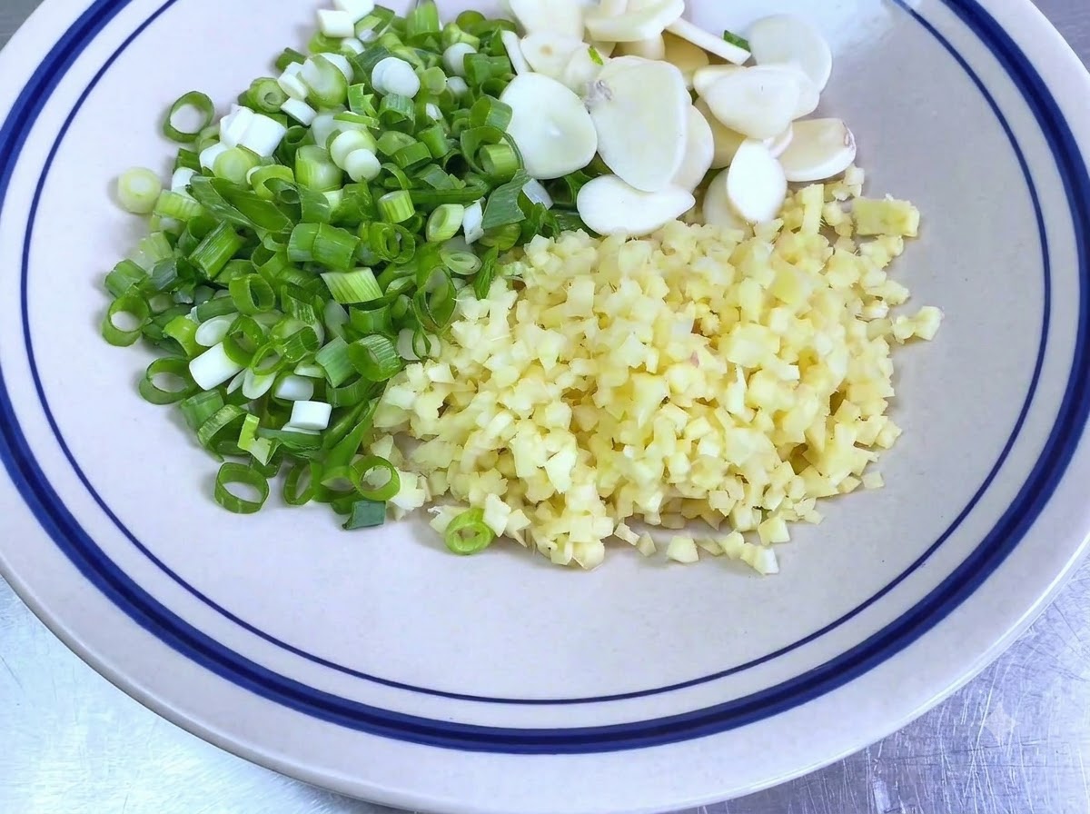 Un cuenco blanco con cebolletas picadas, dientes de ajo en rodajas y jengibre picado.