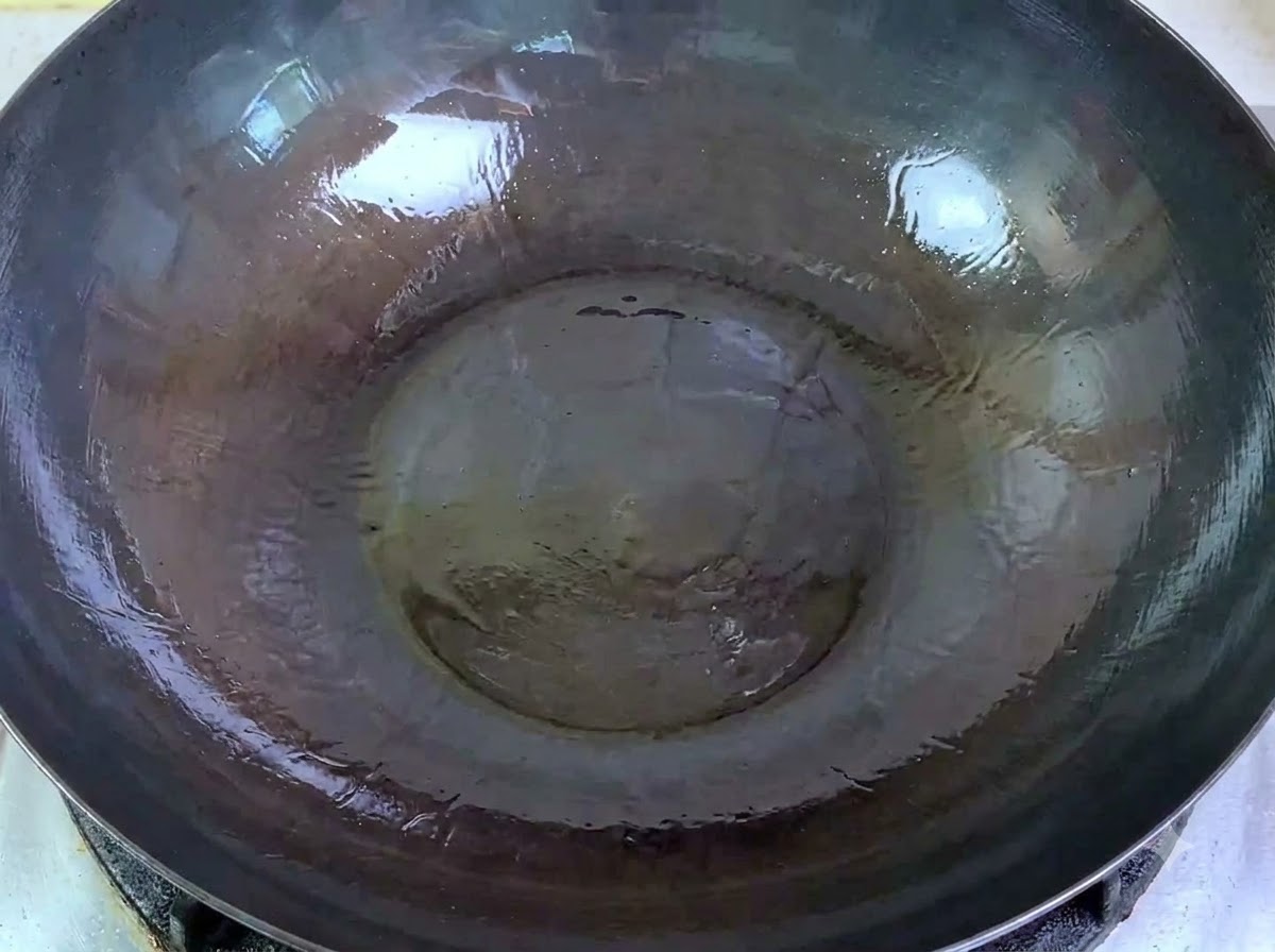 Carne de cerdo cruda picada siendo vertida desde un cuenco a un wok grande con aceite caliente.