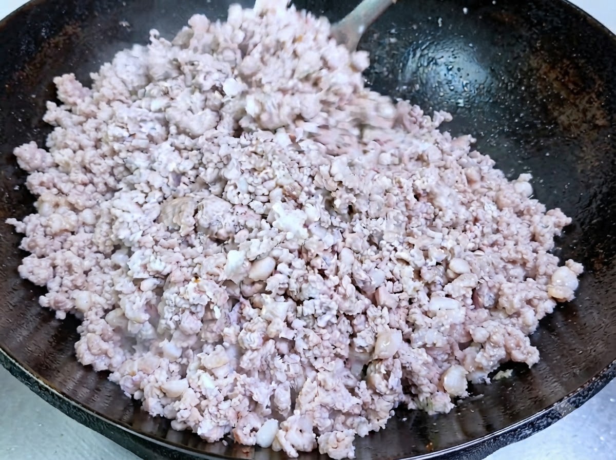 Carne de cerdo picada cocinándose y volviéndose opaca en un wok sazonado.