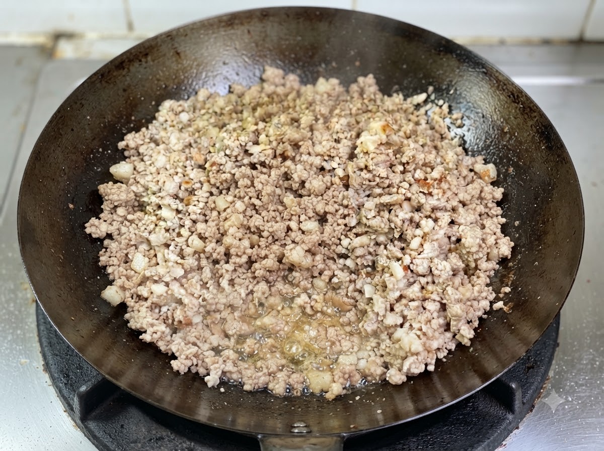 Carne de cerdo picada dorándose en un wok con aceite derretido visible burbujeando en la base.