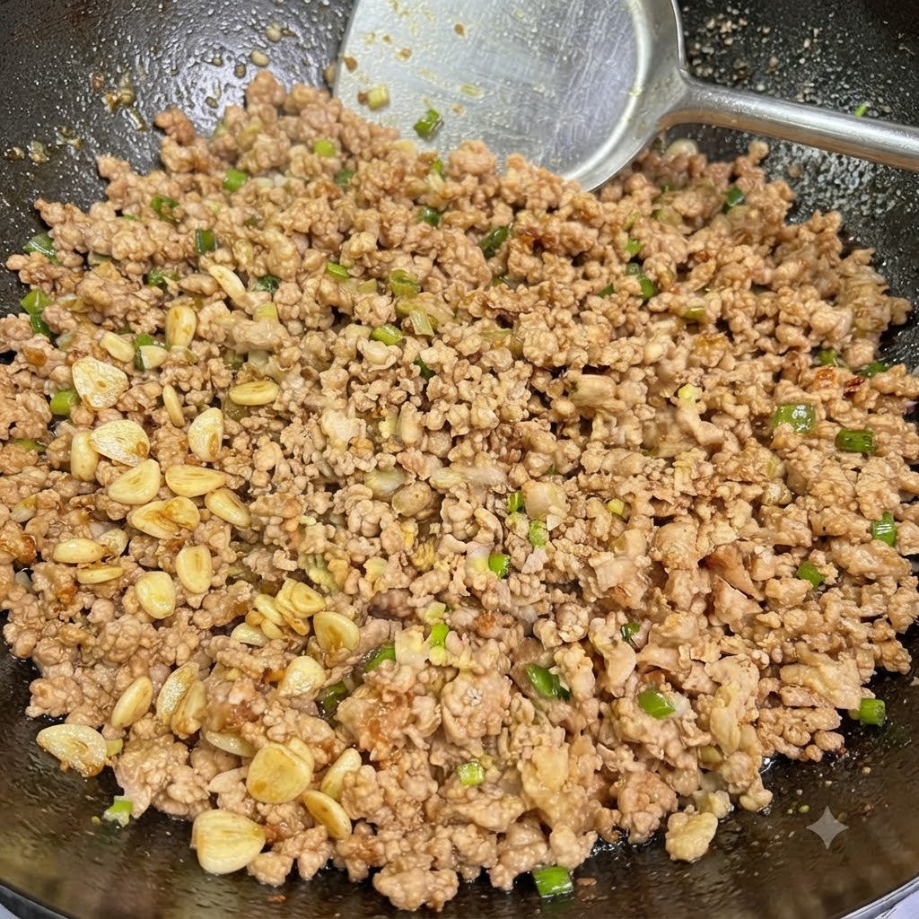 Carne de cerdo picada cocida mezclada con cebolletas y ajo siendo revuelta en un wok con una espátula.