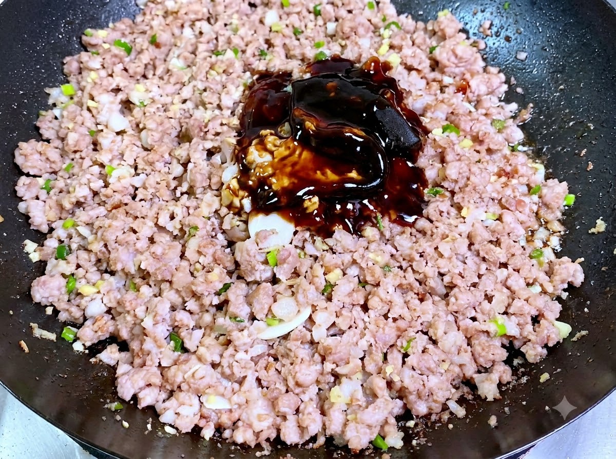 Un montón de pastas y salsas de soja oscuras apiladas directamente sobre la carne de cerdo picada cocida en un wok.
