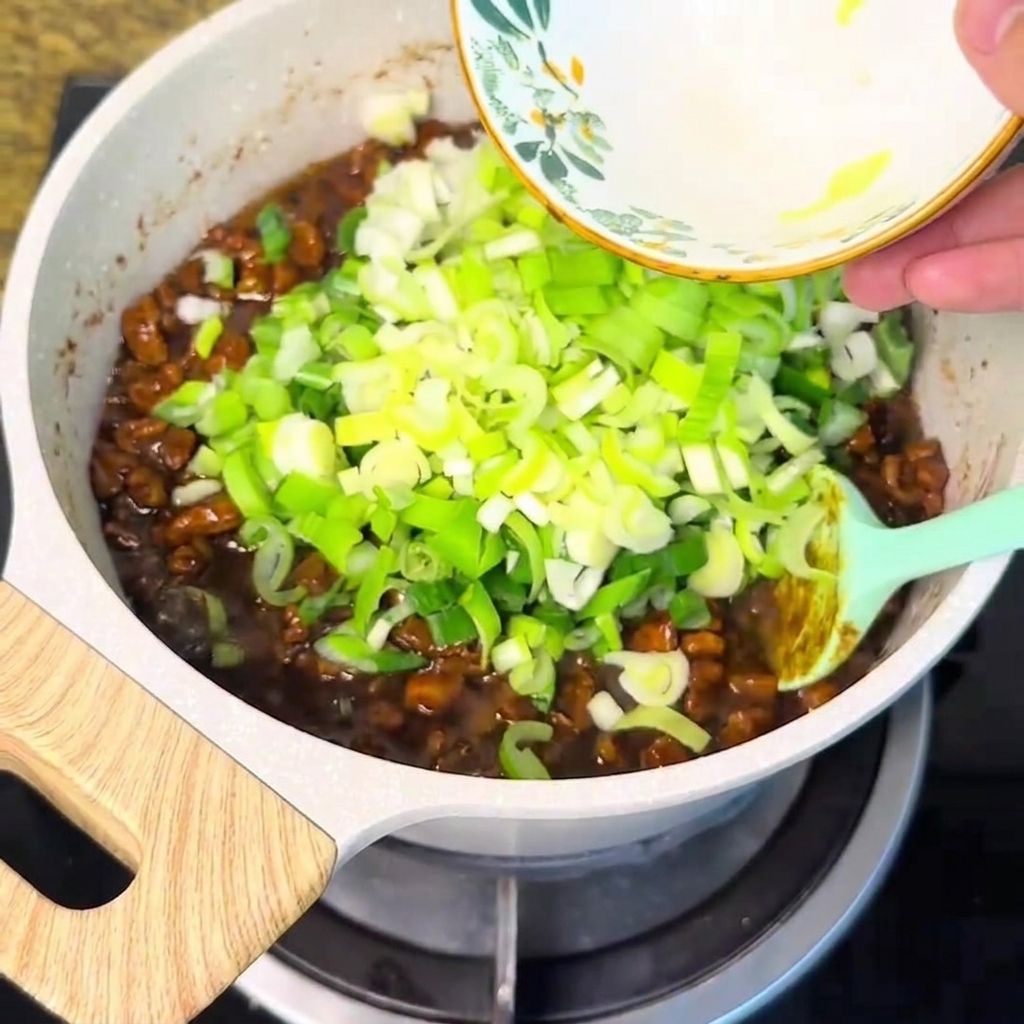 Cebollas verdes picadas vertidas desde un tazón en la salsa de carne burbujeante.