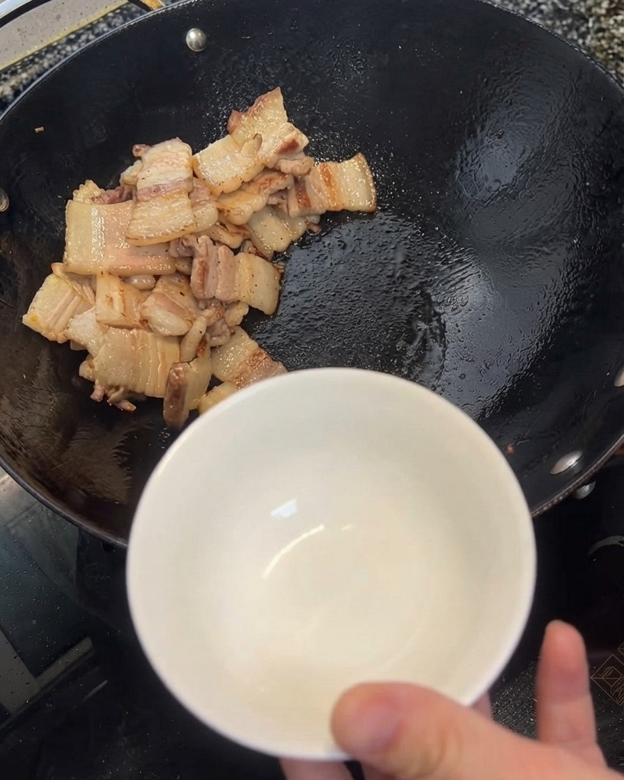 Exceso de aceite siendo retirado del wok a un tazón blanco usando una espátula.
