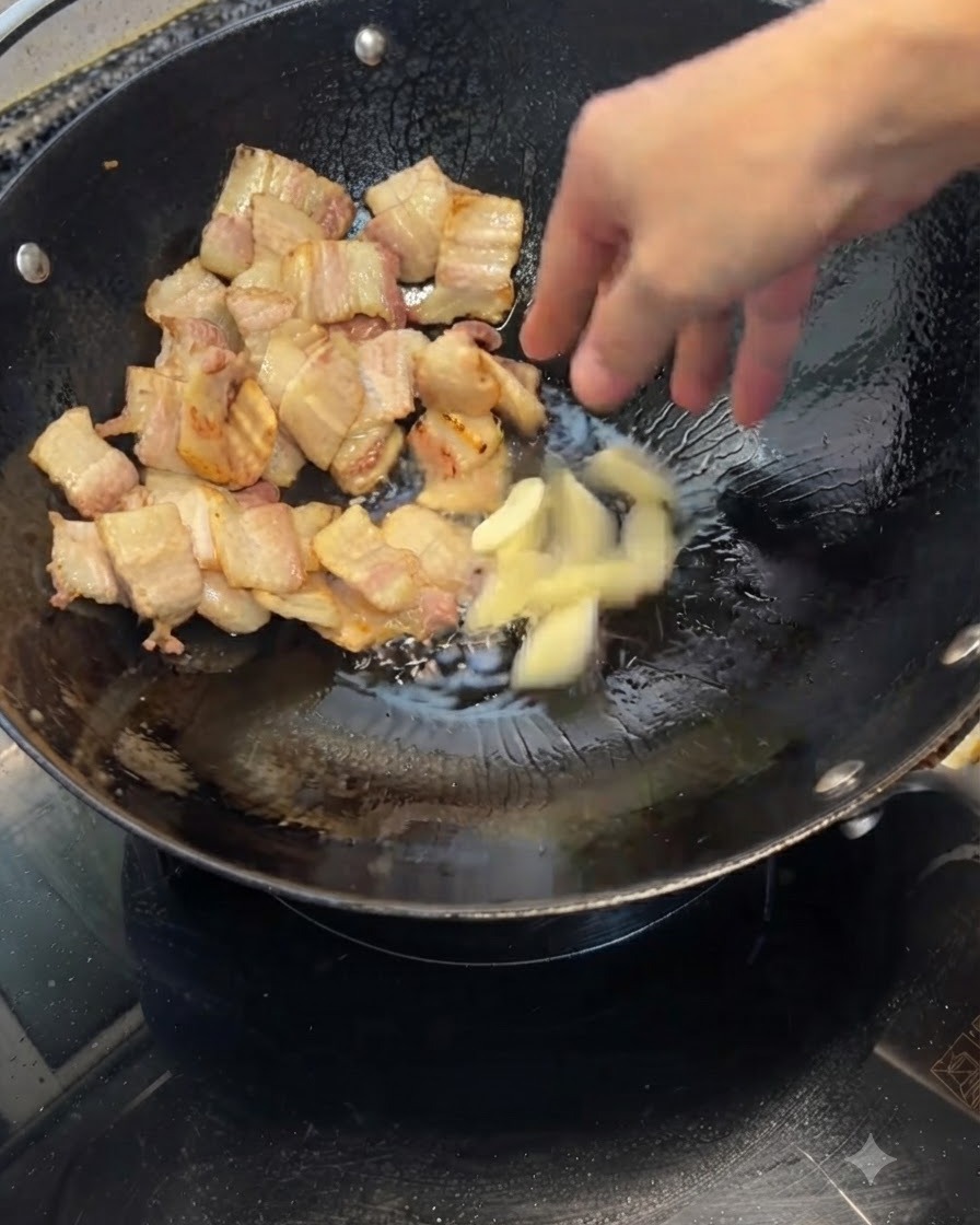 Dientes de ajo machacados siendo arrojados a un wok que contiene trozos de cerdo dorados.