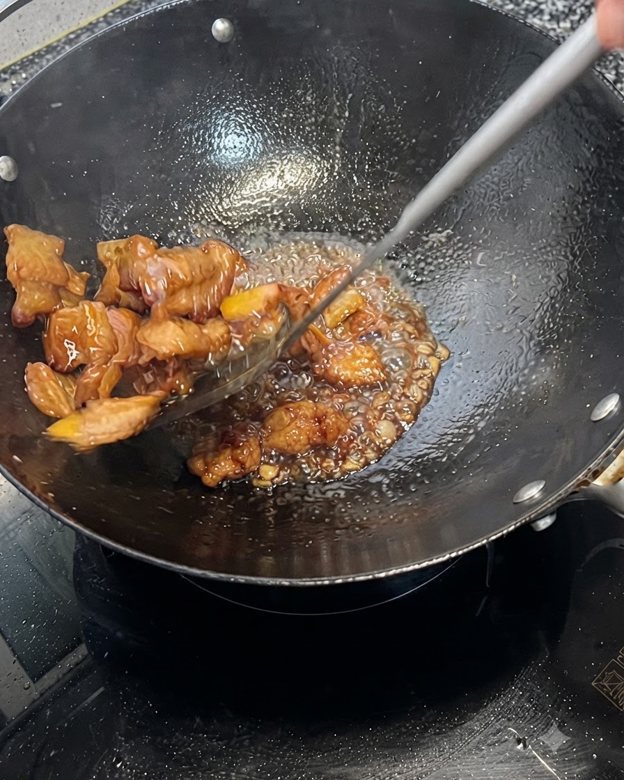 Panza de cerdo siendo mezclada rápidamente y cubierta con una salsa oscura burbujeante en un wok.