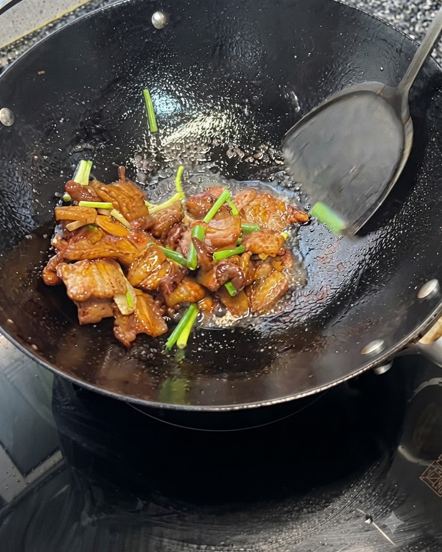 Una espátula mezclando la panza de cerdo y los cebollinos juntos dentro de un wok caliente.